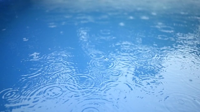 蓝色的水面上有一圈圈的雨滴。抽象的背景。游泳池里的雨。视频素材