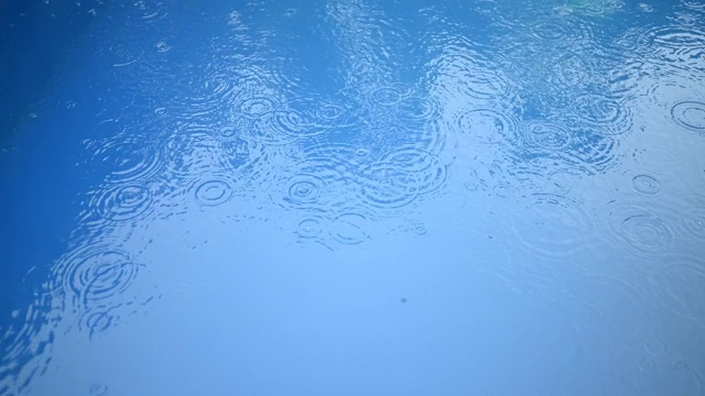 蓝色的水面上有一圈圈的雨滴。抽象的背景。游泳池里的雨。视频素材