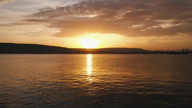 海面在日光下的金色夕阳中鸟瞰无人机在上面滑行。海面上的小波浪。海面上阳光灿烂的日落。太阳。有云的天空。地平线视频素材