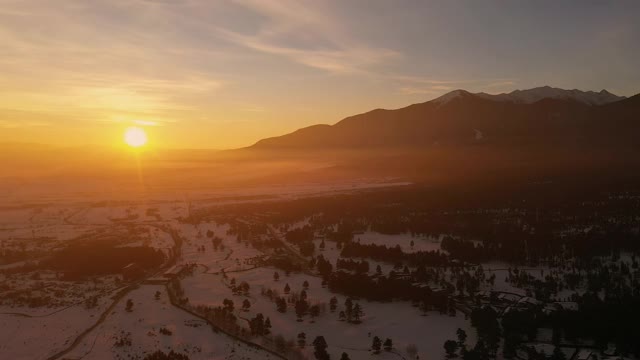 雪峰的全景和在滑雪胜地的屋顶在黎明的清晨鸟瞰滑梯。冬天的早晨阳光明媚。浮动的雾视频素材