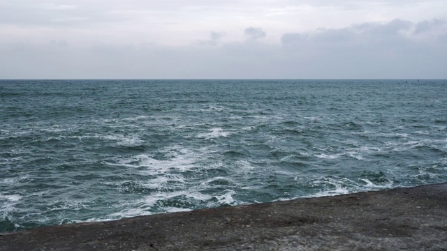 在一个晴朗的冬日里，巨大的海浪拍打着码头，撞击着湛蓝的天空。运动波与飞溅。不安宁的海面。前视图视频素材