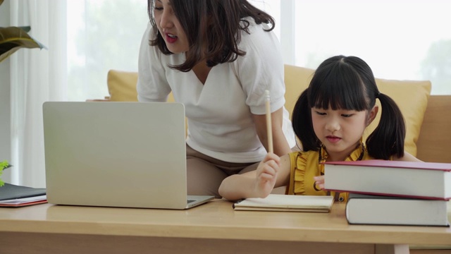 亚洲妈妈教孩子的女儿学习网上从家里，电子学习或自学家庭学校视频素材