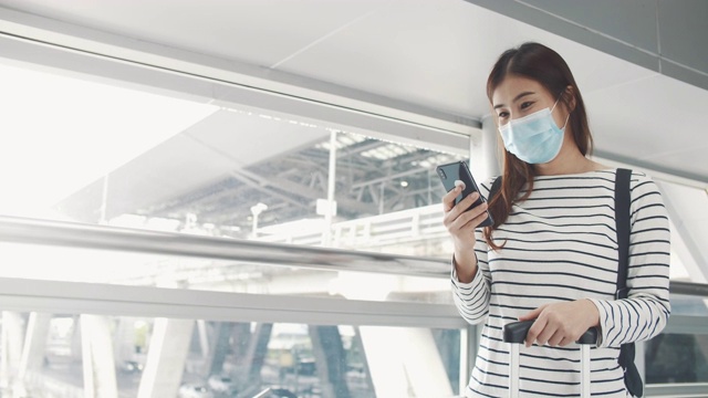 一名年轻女子戴着口罩在机场候机厅使用智能手机视频素材