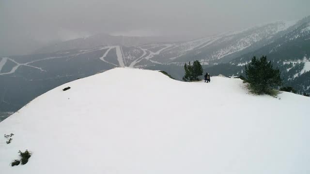 夫妇下着雪，靠近悬崖，四周群山环绕。美丽的雪景与山脉遍布地平线- 4K视频素材