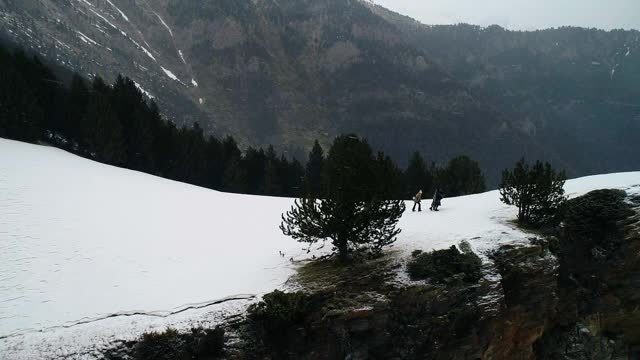 夫妇俩下着雪，走在悬崖边上，四周群山环绕。美丽的雪景与山脉遍布地平线- 4K视频素材