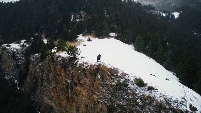 一对情侣看着镜头，在悬崖边互相拥抱，四周群山环绕，在4K白雪下视频素材