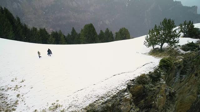 夫妇俩在雪地里散步，从悬崖边回来，四周群山环绕，雪下4K视频素材