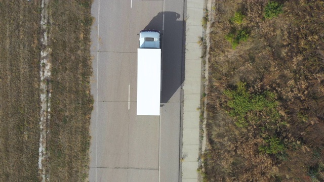 带拖车的卡车在笔直的道路上行驶并运输货物的鸟瞰图。飞过在乡村公路上行驶的运输卡车。货物运输的概念。俯视图视频素材