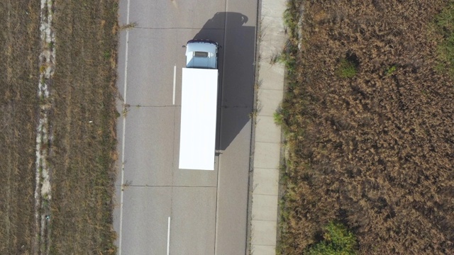 带拖车的卡车在笔直的道路上行驶并运输货物的鸟瞰图。飞过在乡村公路上行驶的运输卡车。货物运输的概念。俯视图视频素材