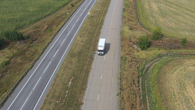 卡车鸟瞰图与货物拖车驾驶在空的道路和运输货物。在乡村公路上飞驰的运送卡车。周边乡村环境优美。慢动作视频素材