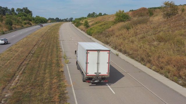 空中拍摄的卡车与货运拖车行驶在道路上的农村环境。在乡村公路上行驶的卡车上飞过。物流配送的概念。高速公路上的交通。后视图视频素材