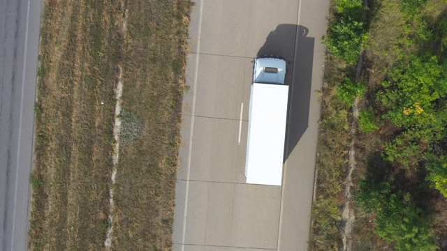 带拖车的卡车在笔直的道路上行驶并运输货物的鸟瞰图。飞过在乡村公路上行驶的运输卡车。货物运输的概念。俯视图视频素材