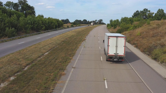 空中拍摄的卡车与货运拖车行驶在道路上的农村环境。在乡村公路上行驶的卡车上飞过。物流配送的概念。高速公路上的交通。后视图视频素材