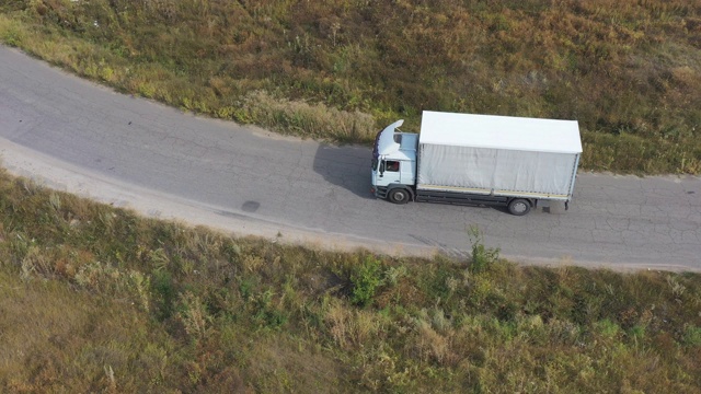 航拍的卡车与货物拖车驾驶在道路上运输货物。在乡村公路上飞驰的运送卡车。工业汽车驶向目的地。物流的概念。视频素材