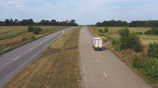 航拍的卡车与货物拖车驾驶在道路上运输货物。在乡村高速公路上飞驰的运货车，周围自然环境优美。后视图视频素材