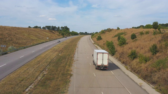 空中拍摄的卡车与货运拖车行驶在道路上的农村环境。在乡村公路上行驶的卡车上飞过。物流配送的概念。高速公路上的交通。后视图视频素材