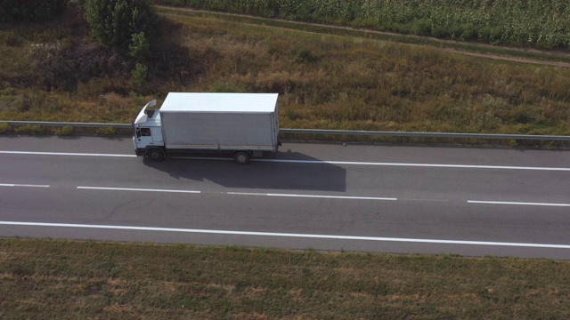 航拍的卡车与货物拖车驾驶在空的直线道路上。飞过乡村公路上行驶的白色卡车。物流和配送的概念。侧视图慢镜头视频素材