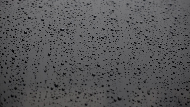 水滴在黑色光滑的表面上近距离流下。雨滴落在光滑的黑色表面上。黑色汽车引擎盖的纹理和雨滴。抽象的黑色背景与雨滴。视频素材