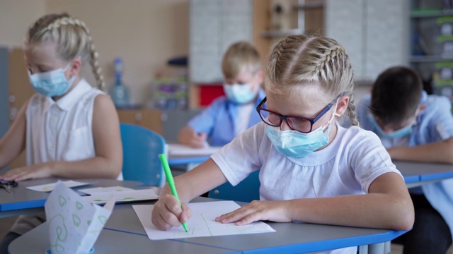 学生们在隔离和禁闭后回到学校，戴眼镜和医用口罩的女学生坐在课桌前做作业视频素材