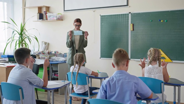 回到学校，戴眼镜的女老师在上课前向学生展示如何戴上医用口罩视频素材