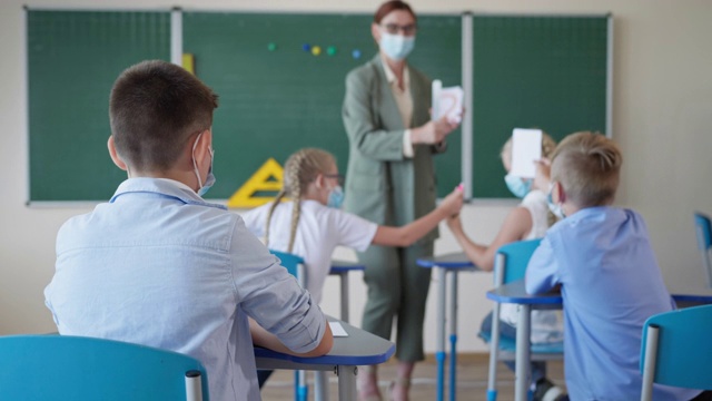 一名戴面具的小学生举手回答老师的问题，学生们坐在课桌前上课视频素材