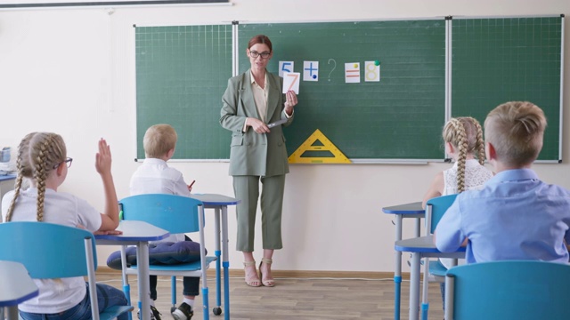 小学课堂上，女老师在黑板旁向一群孩子展示写有数字的卡片视频素材