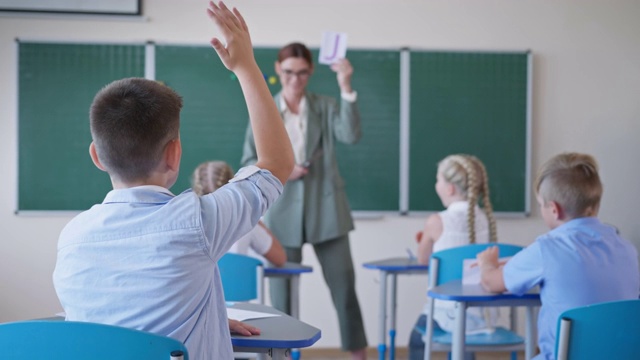 在学校上课时，老师向学生展示印有字母的卡片，学生站在教室前面，专心听讲，并举手示意视频素材