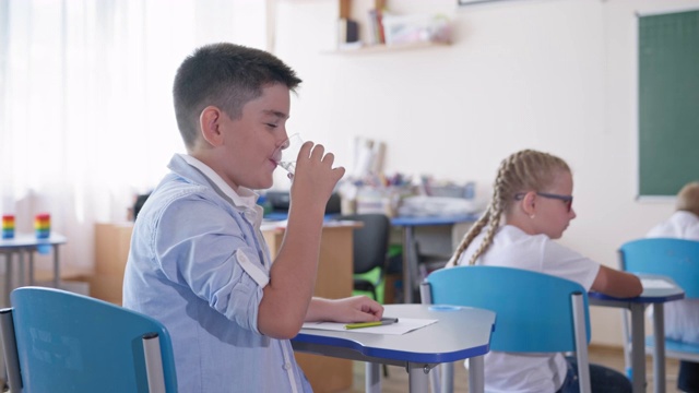 小学生在课堂上坐在课桌边喝水，背景是同学，小学视频素材