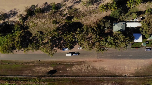 一辆汽车拖着一辆大篷车沿着昆士兰北部的布鲁斯高速公路行驶，沿途是退潮时美丽的海滩。地平线上的岛屿沐浴在金色的阳光下视频素材