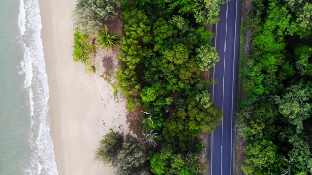 汽车和卡车在郁郁葱葱的雨林之间的一条小路上行驶，旁边是热带金色的沙滩。摄于昆士兰北部凯恩斯郊外视频素材