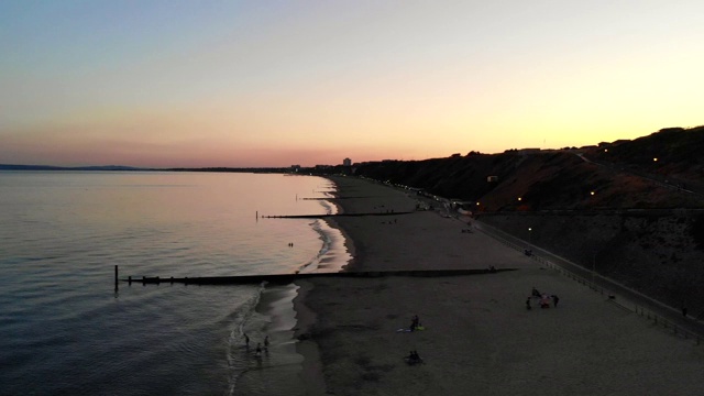 美丽的夏日日落在海滩上。黄色、粉色和蓝色的色调沐浴着天空，日落在悬崖后面，使海洋表面闪闪发光视频素材