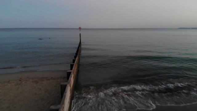 向大海驶去，经过一个长长的岸边漂木坝。淡淡的夏夜阳光沐浴在柔和的蓝色海洋，它在下面闪闪发光视频素材