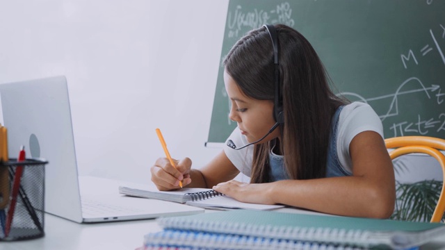 女学生在耳机书写和显示笔记本，同时在线学习在家视频素材