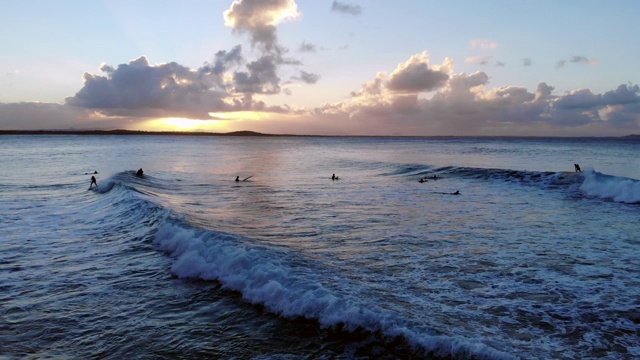 冲浪者骑在完美的波浪沿着努萨头海岸在澳大利亚的阳光海岸，太阳下山后的山在地平线上视频素材