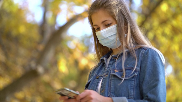 肖像妇女戴着医用防护口罩走在街上使用手机短信滚动浏览互联网搜索第二波新冠病毒防护大流行的新闻。视频素材