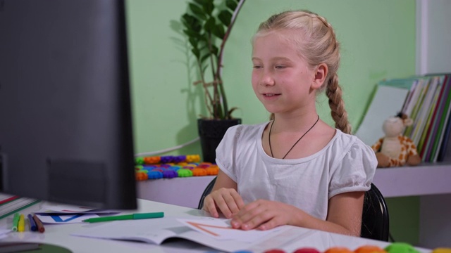 小学生在家接受教育，可爱聪明的女孩手里拿着卡片在电脑上观看在线数学课，并在流感期间在房间里做笔记视频素材