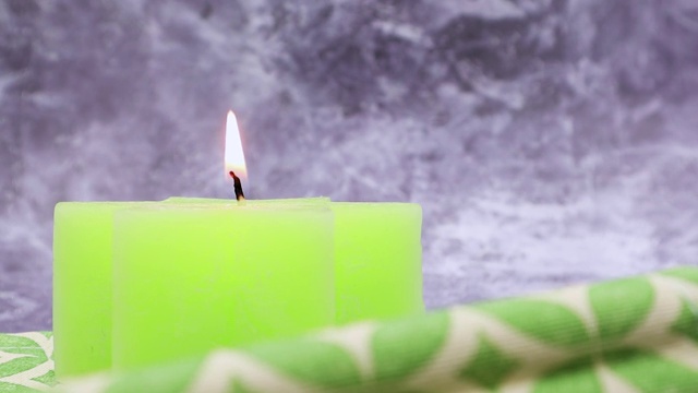 一根绿色的点燃的蜡烛放在桌子上，绿色的亚麻布餐巾放在美丽的灰色大理石背景上。放置你的文本。圣诞装饰品视频素材