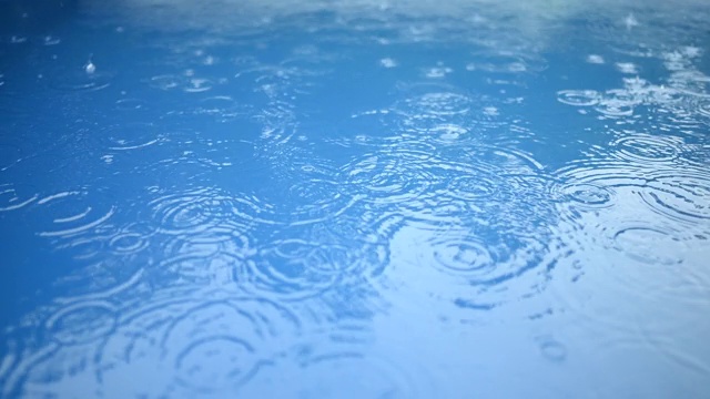 蓝色的水面上有一圈圈的雨滴。抽象的背景。游泳池里的雨。视频素材