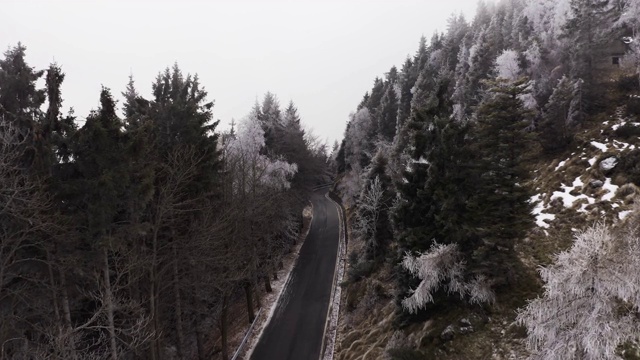 鸟瞰图的汽车驾驶在一个雾天的山区。汽车在弯弯曲曲的道路上行驶，附近有白雪皑皑的树木。慢动作视频素材