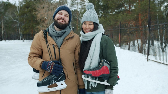 亚洲女人和白人男人在雪地里拿着溜冰鞋的慢动作肖像视频素材