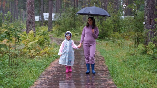 小女孩和妈妈在秋天的雨天里散步视频素材