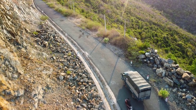 空中跟踪卡车和摩托车在悬崖边的山路上行驶。视频素材