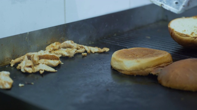 快餐，一个汉堡包的烹饪过程，一个厨师用手套在烤架上煎肉和小面包来制作美味多汁的汉堡，手的特写视频素材