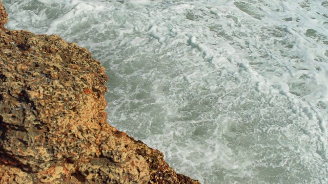 海浪拍打着岩石海岸，绿色的水溅起浪花，产生白色的泡沫，慢动作视频视频素材