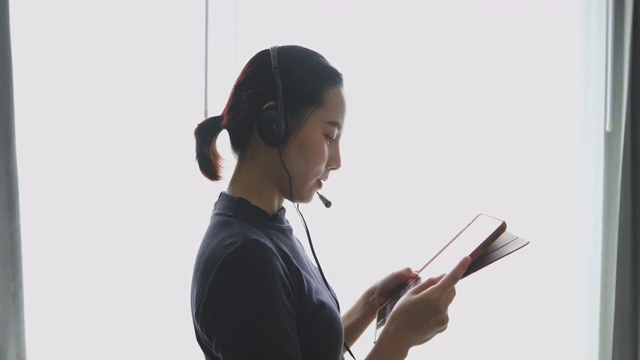 亚洲女性戴着耳机，用数字平板电脑视频开会，在家开会视频素材