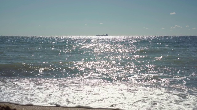 货船停泊在海上地平线上。从沙滩上看，海水闪烁着光芒视频素材