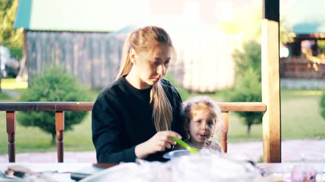 年轻漂亮的妈妈正在给女儿喂粥，他们坐在避暑的房子里。视频素材