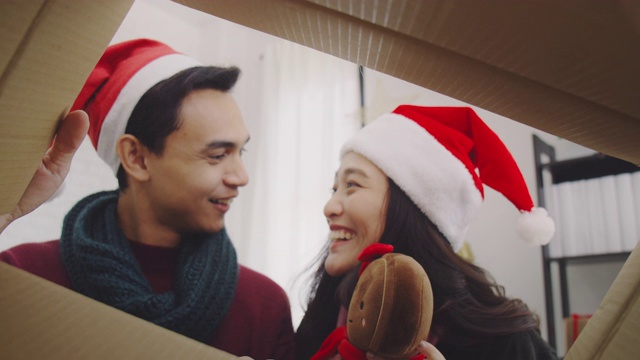 年轻的亚洲夫妇打开礼盒，用手把礼物从盒子在圣诞节和新年期间在家里的背景。圣诞节庆祝活动的概念。4 k慢动作。视频素材