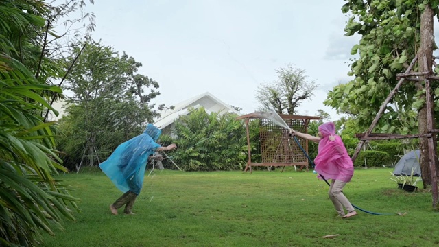 幸福的情侣在爱穿着粉红色和蓝色的雨衣，在雨中玩，在后院打转呆在家里。视频素材