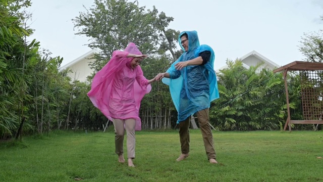 幸福相爱的情侣穿着粉色和蓝色的雨衣，在雨中玩耍。缓慢的运动。视频素材